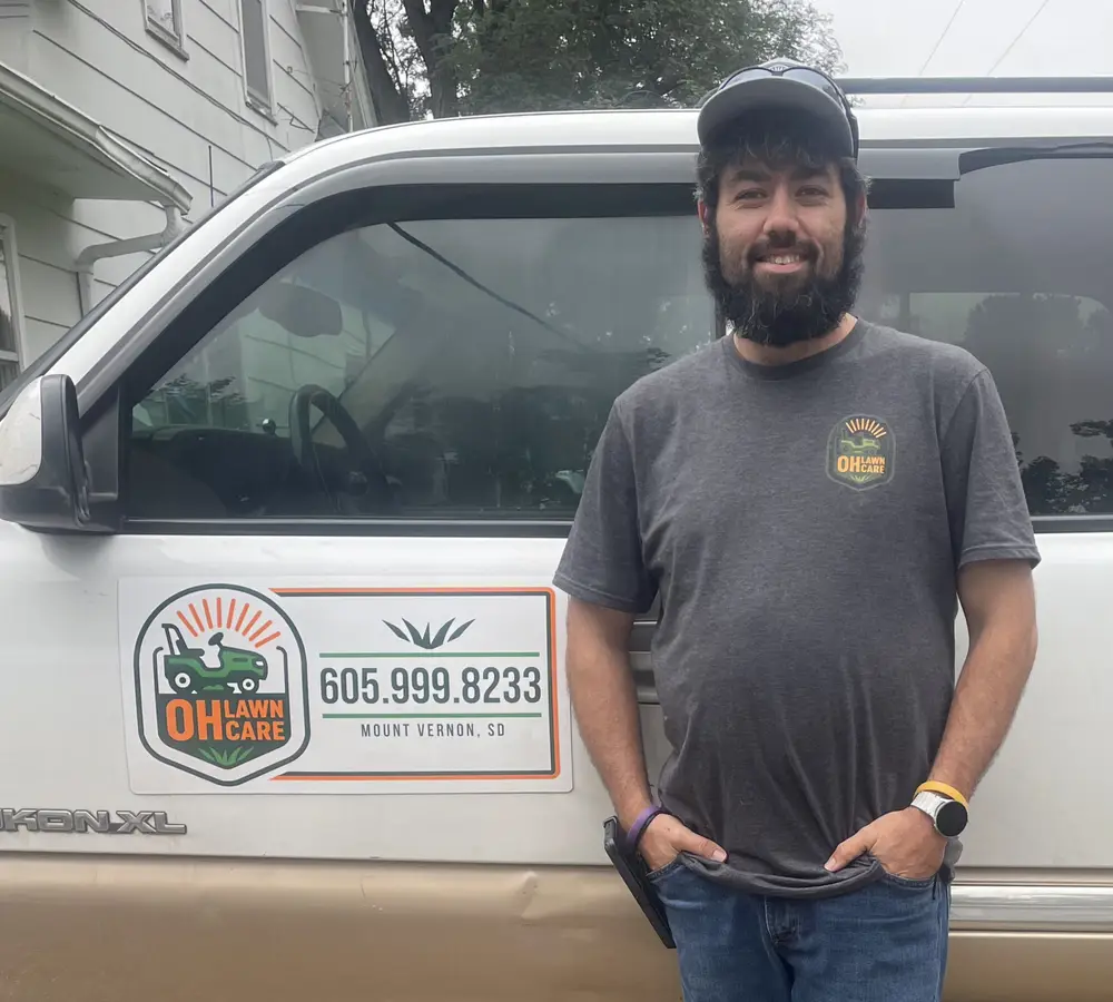 Jared Olsen, owner of OH Lawn Care, standing beside his signwritten GMC Yukon XL in Mount Vernon