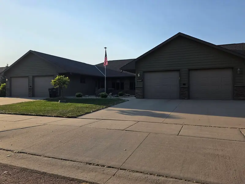 A mown lawn beside a wide concrete driveway at a home with three garage doors