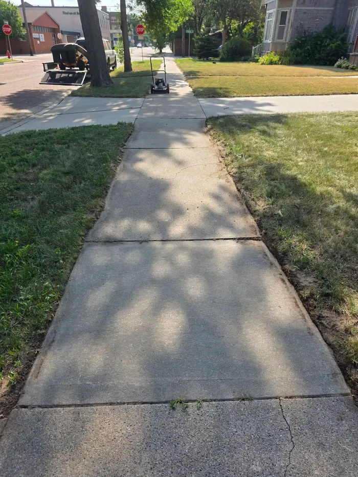 A sidewalk with the grass trimmed clean along both edges